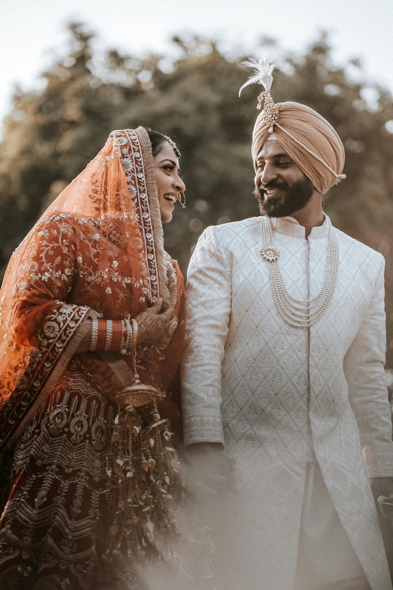 A Punjabi Sikh bride and groom smiling at each other, wearing traditional wedding attire